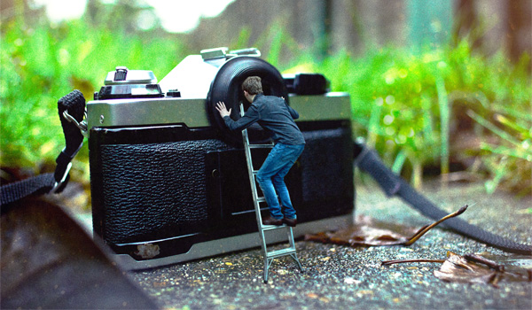 Der kleine Mann nutzt eine Leiter, um durch das Auge einer Kamera zu schauen.