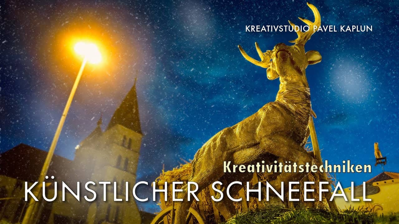 Goldene Hirschstatue mit fallendem Schnee und einem Haus dahinter